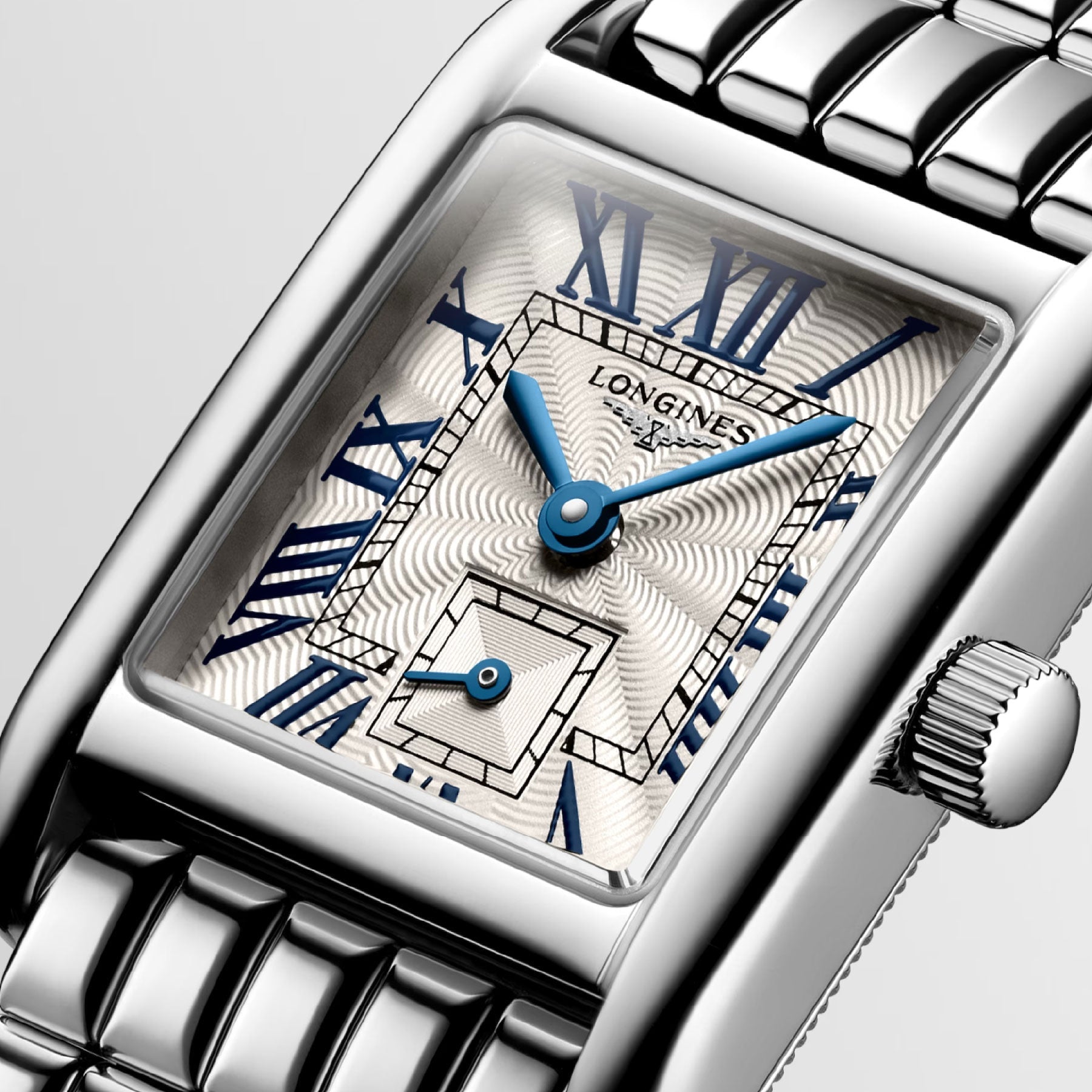 The Longines Mini Dolcevita Quartz 21.5 x 29mm Watch features a rectangular face housed in a stainless steel case. It showcases a patterned cream dial with sophisticated blue Roman numerals and hands, along with a small square subdial. The dial is elegantly accented by the Longines brand name and paired with a stylish metal link bracelet.