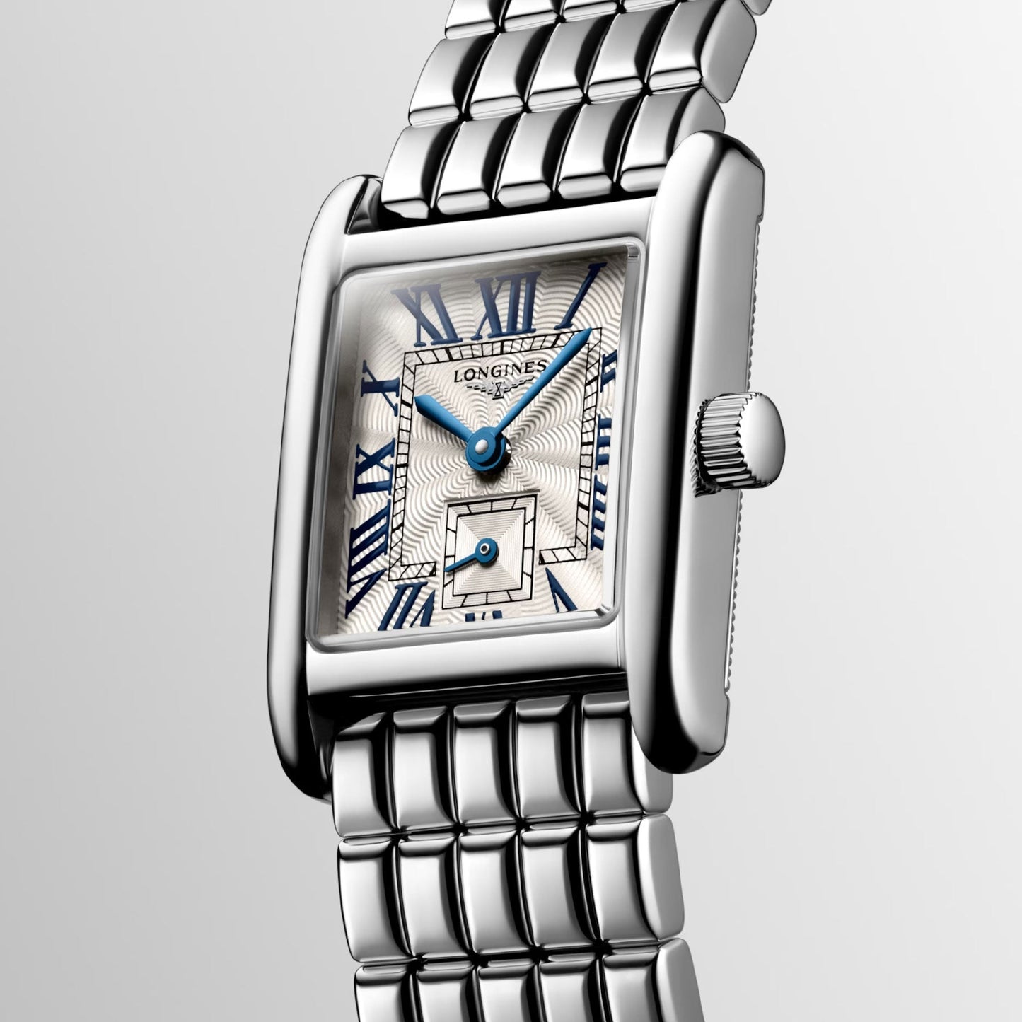 The Longines Mini Dolcevita Quartz 21.5 x 29mm Watch is a stylish silver wristwatch characterized by its rectangular face and metallic strap. It features Roman numerals, blue hands, and a small secondary dial, while the brand name is elegantly displayed against a gradient of light gray on its stainless steel case.