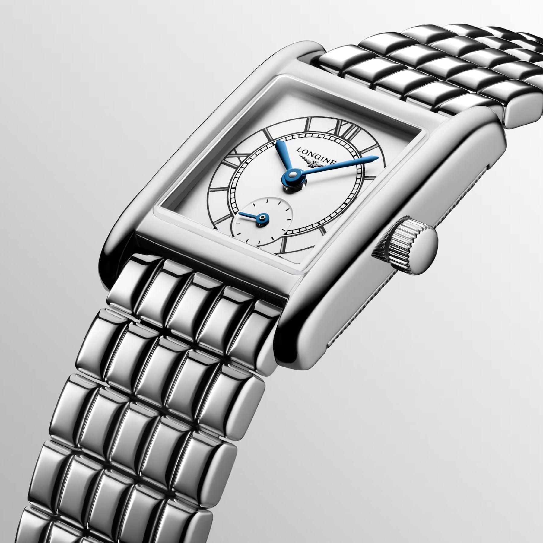 A close-up of a Longines Mini Dolcevita Quartz 21.5 x 29mm watch showcases its rectangular shape, metallic strap, and stainless steel case. The watch has a white face complemented by blue hands and embodies sleek, classic design elements, with the Longines brand name elegantly displayed on the face.