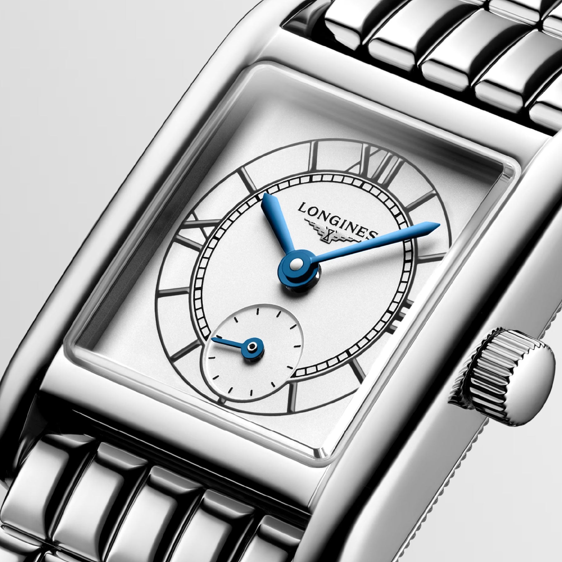 A close-up of the Longines Mini Dolcevita Quartz 21.5 x 29mm watch highlights its rectangular stainless steel case paired with a polished metal band. The dial features blue hour and minute hands, Roman numerals on a white background, and a small seconds subdial. The Longines brand name is elegantly displayed on the face.