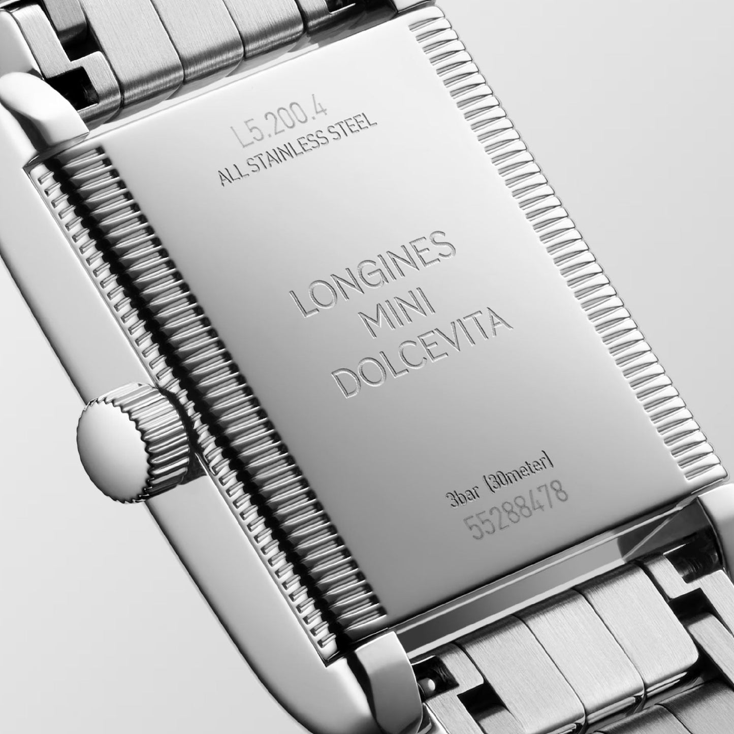 A close-up of the Longines Mini Dolcevita Quartz 21.5 x 29mm watch highlights its stainless steel case and bracelet, with detailed engravings featuring the model and serial numbers as well as water resistance information.