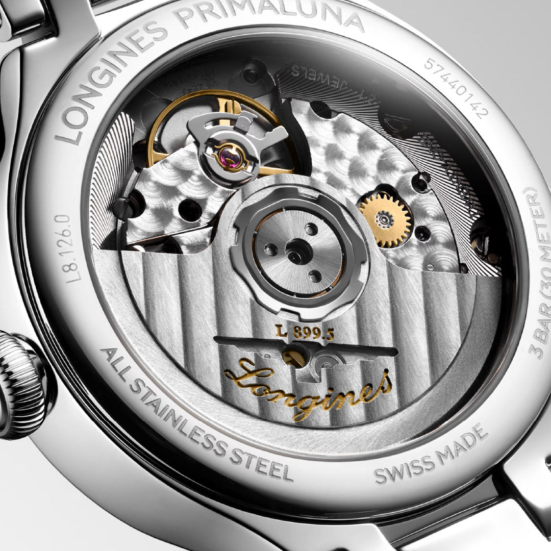 Close-up of the transparent case back of the Longines Primaluna Moonphase Automatic 34mm Watch, highlighting its intricate mechanical movement, visible gears, and engraved gold details. Branding and specifications encircle the edge.