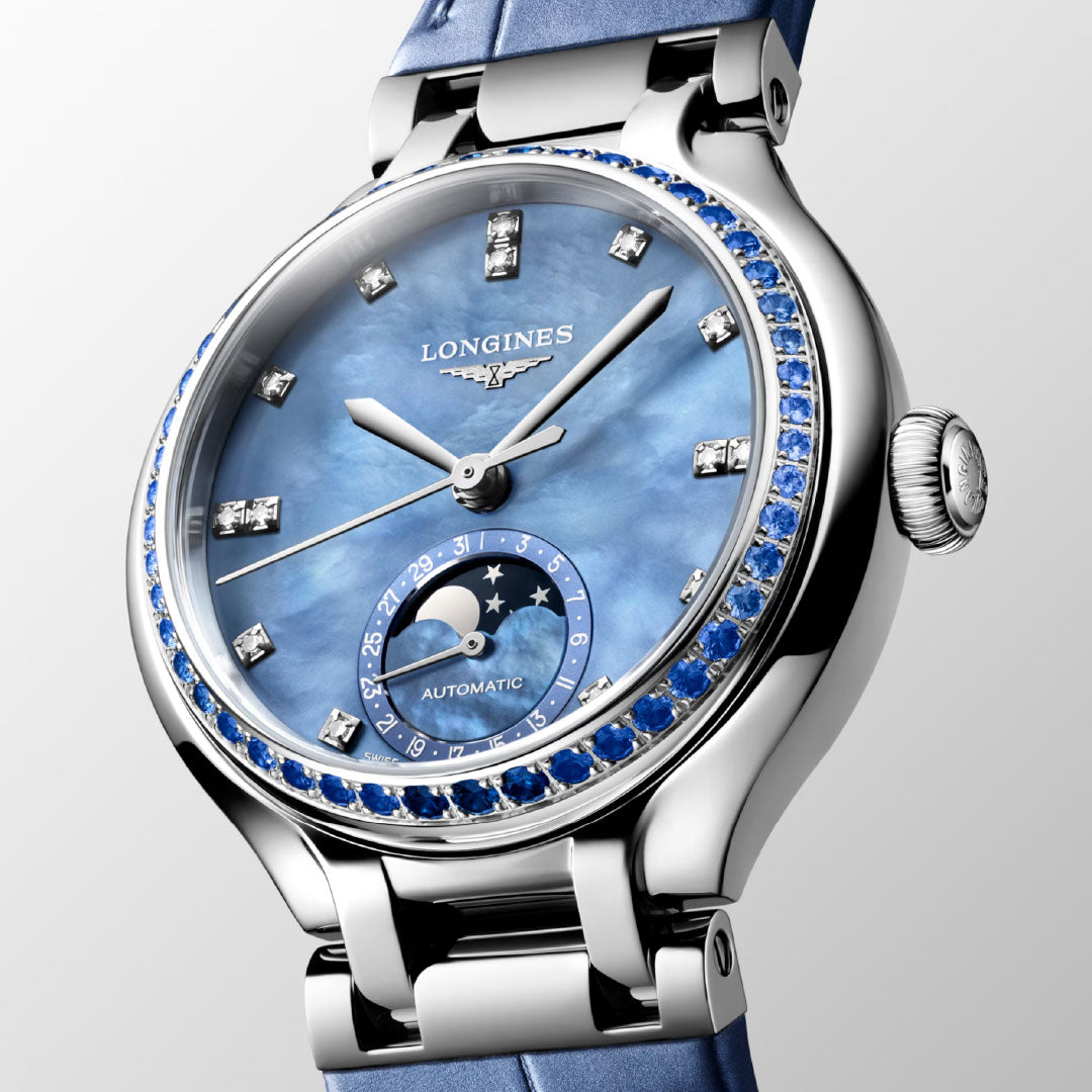 The Longines PrimaLuna Moonphase Automatic 34mm Watch for women features a blue mother-of-pearl dial, diamond hour markers, a sapphire-set bezel, moon phase display, and a blue leather strap—elegantly showcased on a light background.