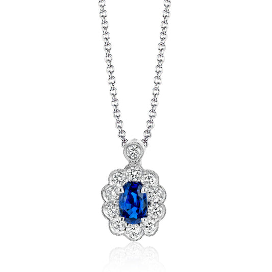 The Simon G. 18K White Gold Sapphire and Diamond Necklace Pendant, by the renowned brand Simon G, features a breathtaking design centered around a vivid blue sapphire encircled by an array of delicate diamonds arranged in a floral pattern.