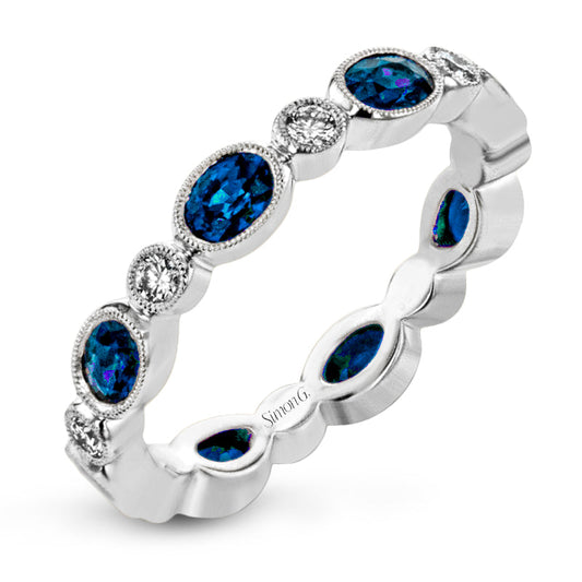 This elegant 18K white gold ring by Simon G. features alternating oval blue sapphires and round diamonds, all set within a refined band enhanced with intricate milgrain detailing.