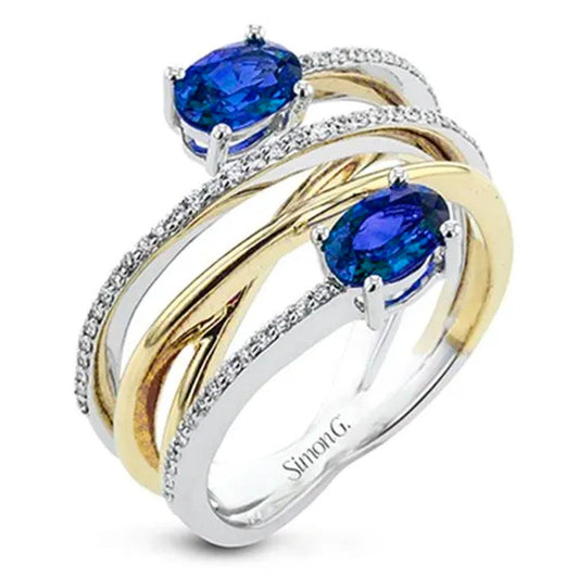 A dual band ring by Simon G, showcasing intertwined 18k white and yellow gold bands embellished with two blue spinel gemstones and small diamonds.