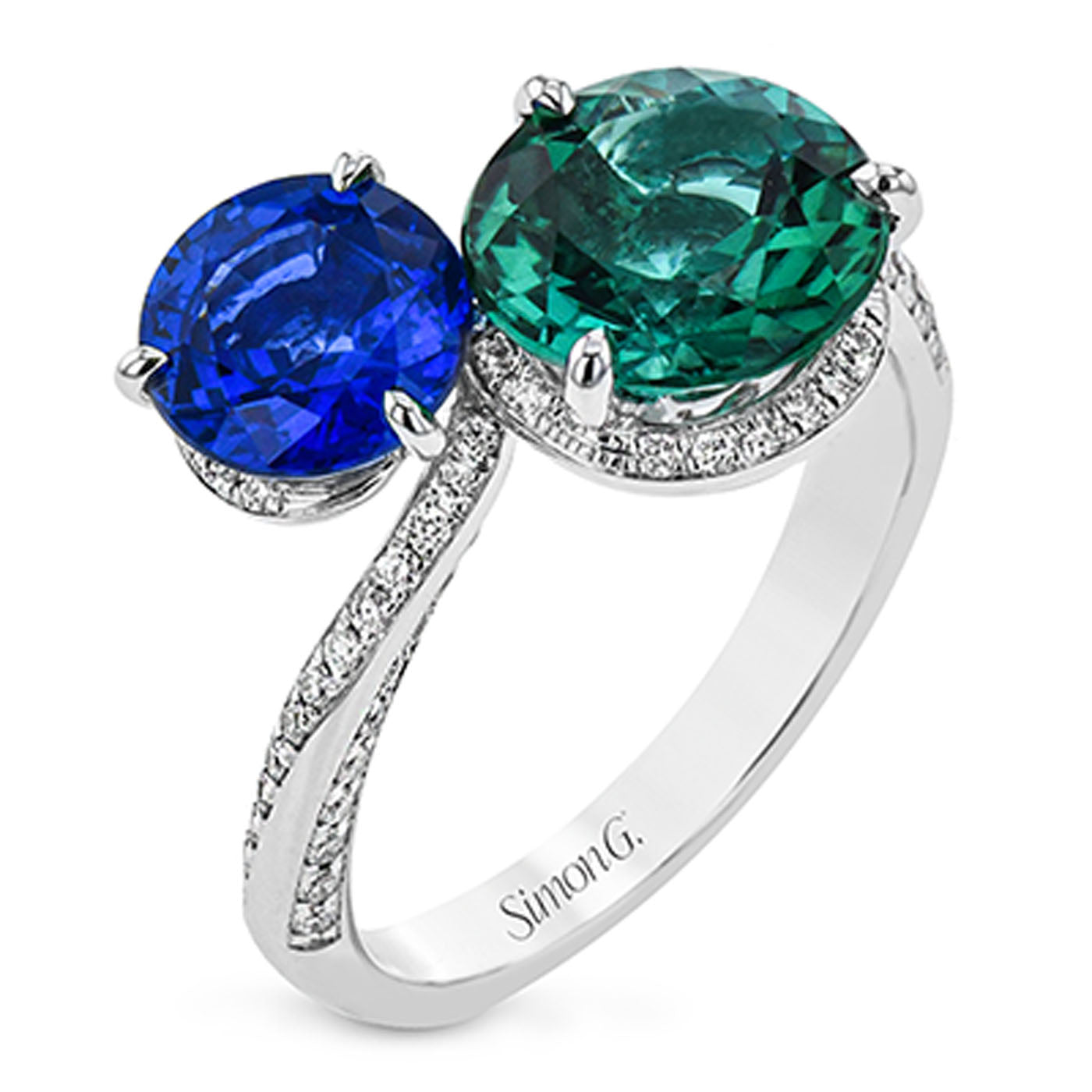 The Simon G. 18K White Gold Tourmaline and Sapphire with Diamond Ring features two prominent round gemstones—a green tourmaline and a blue sapphire—set side by side, with the band embellished with small, clear diamonds for added sparkle and elegance.