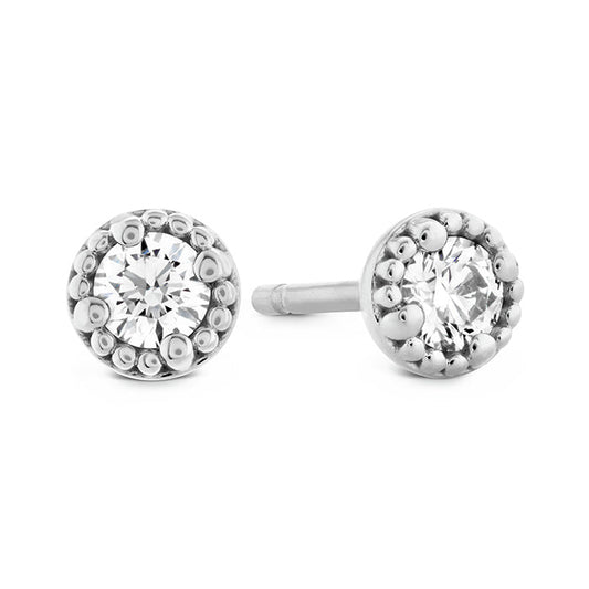 The Hearts On Fire Liliana Milgrain Stud Earrings, crafted in elegant 18 Karat white gold, showcase central round, sparkling gemstones encircled by a decorative beaded design with exquisite milgrain detailing. These earrings are beautifully displayed against a white background.
