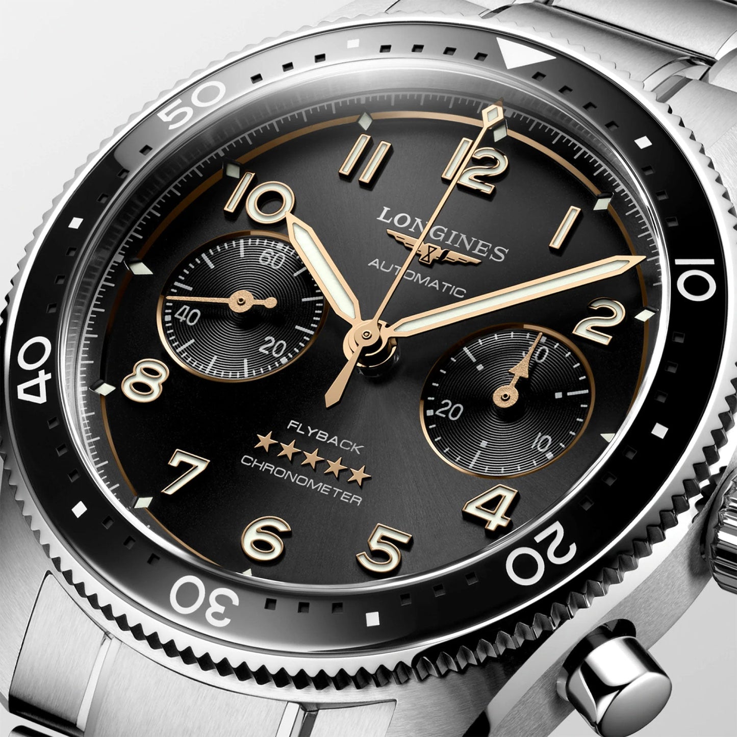 Photograph showcasing the elegant Longines Spirit Flyback Automatic Chronograph 42mm watch. This luxurious timepiece features a silver metal band and a black dial with golden hands, hour markers, and three subdials. The face displays the words "Longines," "Automatic," and "Flyback Chronometer." Originating from the renowned legendary pioneers collection by Longines, known for its winged hourglass logo, it includes a polished bezel with minute markings.