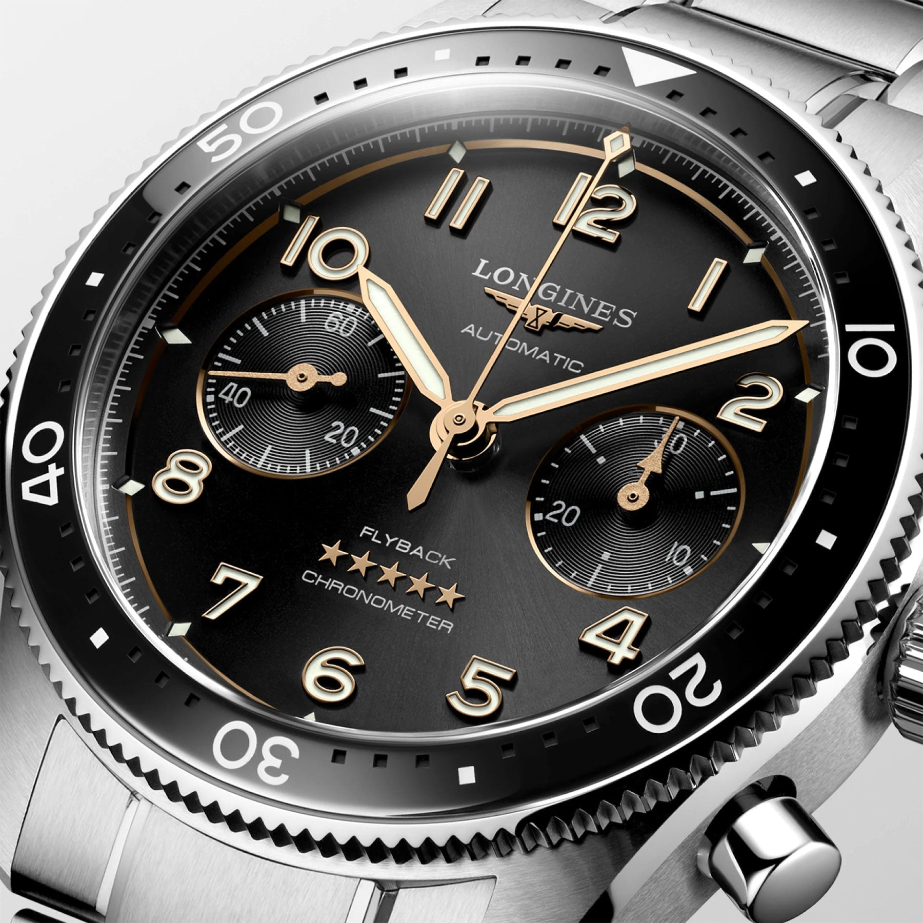 Photograph showcasing the elegant Longines Spirit Flyback Automatic Chronograph 42mm watch. This luxurious timepiece features a silver metal band and a black dial with golden hands, hour markers, and three subdials. The face displays the words "Longines," "Automatic," and "Flyback Chronometer." Originating from the renowned legendary pioneers collection by Longines, known for its winged hourglass logo, it includes a polished bezel with minute markings.
