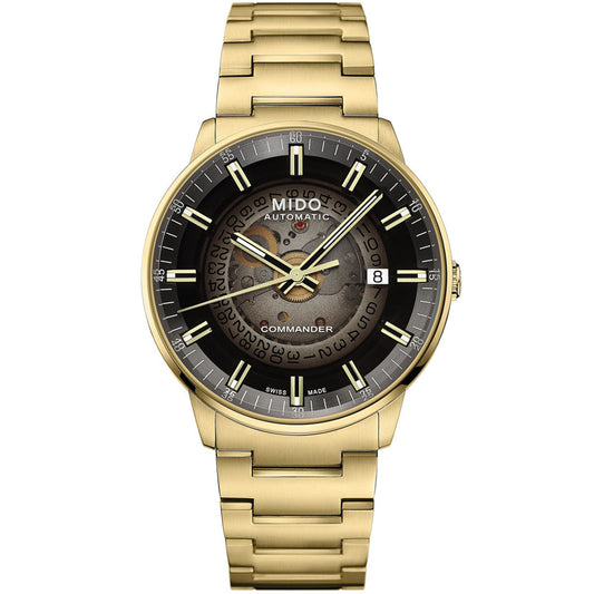 The MIDO Commander Gradient Automatic 40mm Watch features a gold finish, transparent acrylic dial with black and gold details, Caliber 80 movement, date at 3 o'clock, Swiss Made text, skeleton face revealing gears, and a matching gold bracelet.