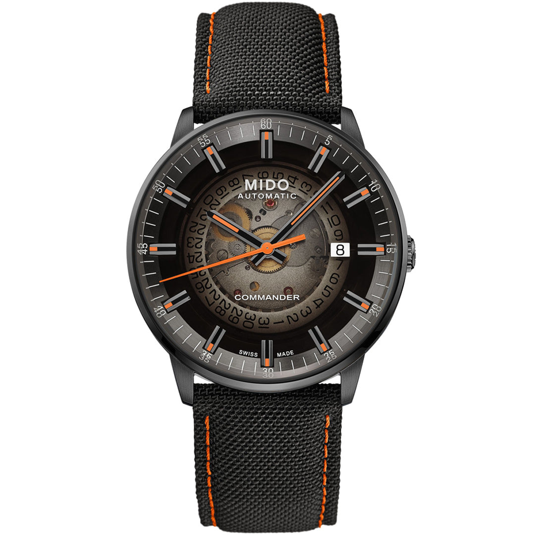 The MIDO Commander Gradient Automatic 40mm Watch features a black textured strap with orange stitching, a transparent dial showing gears, silver hour markers, orange hands, Caliber 80 movement, date at 3 o’clock, and “Commander” above 6.