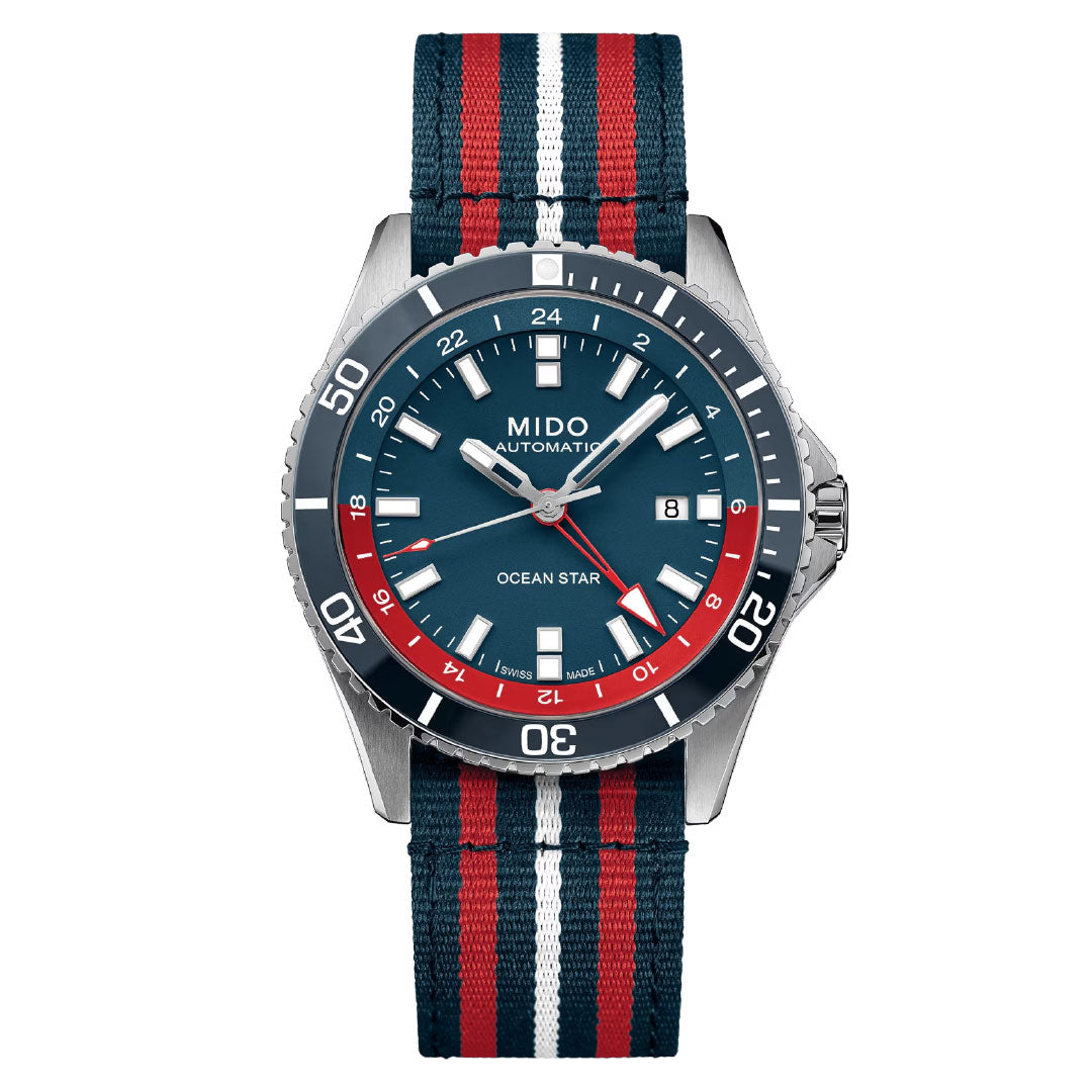 The MIDO Ocean Star GMT Automatic 44mm Watch features a blue dial with white and red accents, date display, and a striped blue/red/white nylon strap. Its stainless steel case and marked bezel show MIDO’s classic diving watch design.