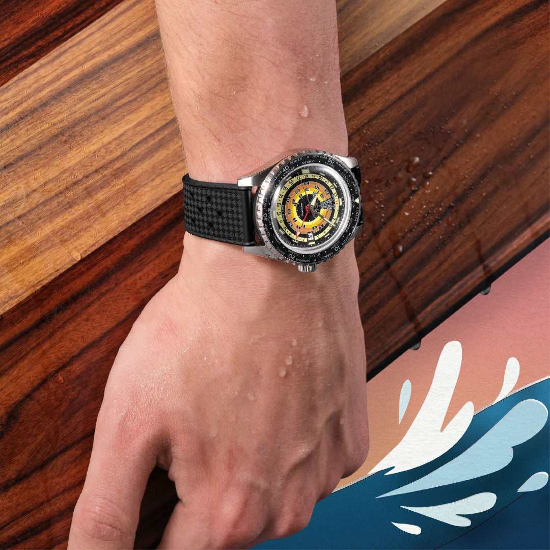 A close-up of a wrist wearing the MIDO Ocean Star Decompression World Timer Automatic 40.5mm, featuring a colorful dial and GMT function, with water droplets on the hand, set against wood and a stylized wave illustration.