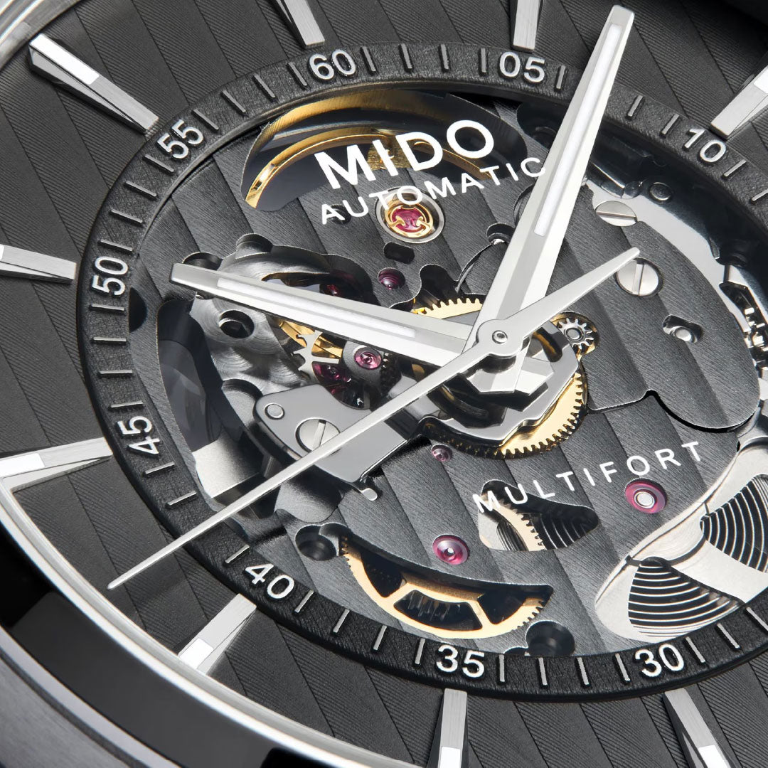 Close-up of the MIDO Multifort Skeleton Vertigo Automatic 42mm Watch, highlighting Swiss craftsmanship and its automatic movement with exposed gears, white hands, and hour markers through a partially open dial.