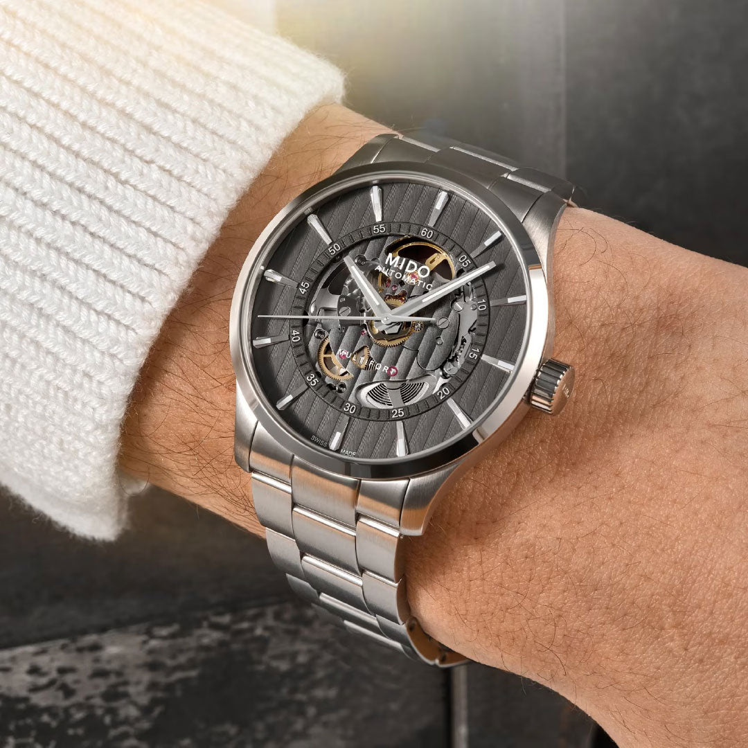 A close-up of a person wearing the MIDO Multifort Skeleton Vertigo Automatic 42mm Watch, featuring a visible skeleton dial with intricate gears, paired with a white ribbed sweater.
