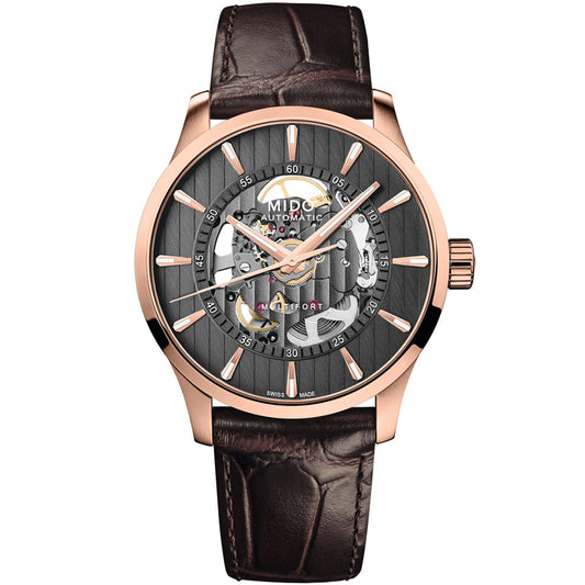 The MIDO Multifort Skeleton Vertigo Automatic 42mm Watch features a rose gold case, brown leather strap, and a partially open black dial that reveals its intricate automatic movement and striking gold accents.