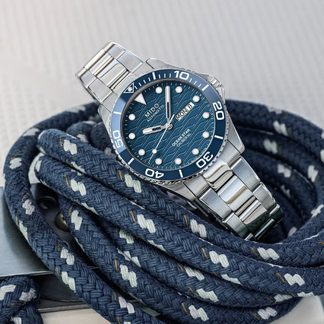 The MIDO Ocean Star 200C Automatic 42.5mm Watch is shown on coiled navy blue rope with white accents, resting on a light-textured surface. The stainless steel timepiece features a blue ceramic bezel and automatic movement.