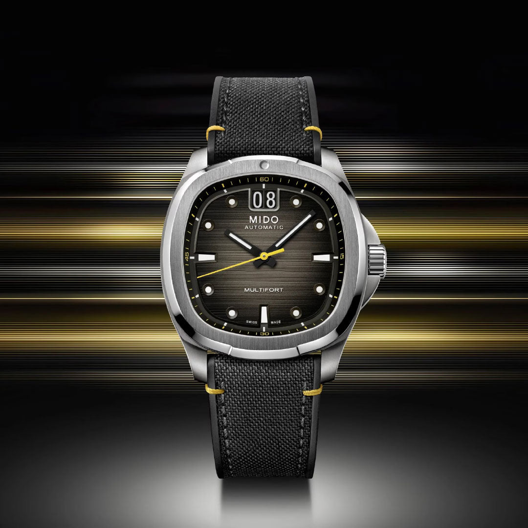 The MIDO Multifort TV Big Date Automatic 40mm Watch showcases a black textured strap, metal case, and black dial by MIDO, set against horizontal gold and silver light streaks.