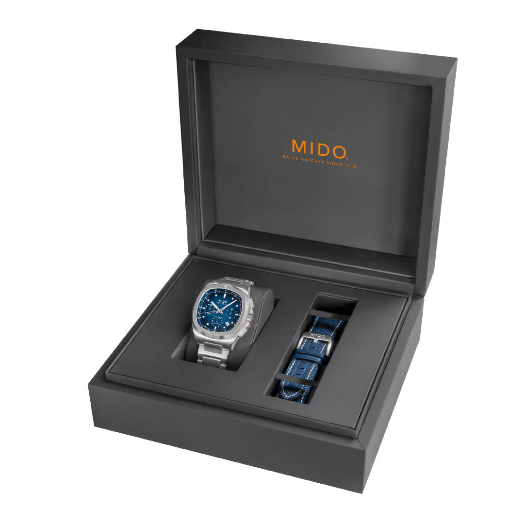 The MIDO Multifort TV Chronograph Automatic 42mm watch in silver with a blue dial is displayed in an open black box with the MIDO logo inside the lid and comes with a matching blue strap.