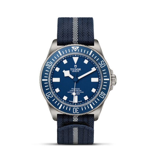 Introducing the TUDOR Pelagos FXD, a sleek blue timepiece designed for professional use. It features a round blue dial with striking white hour markers and a rotating bezel, complemented by a blue and gray striped fabric strap. The durability of this watch echoes that of the Military Submariner, with "TUDOR Geneva" elegantly inscribed on the dial.