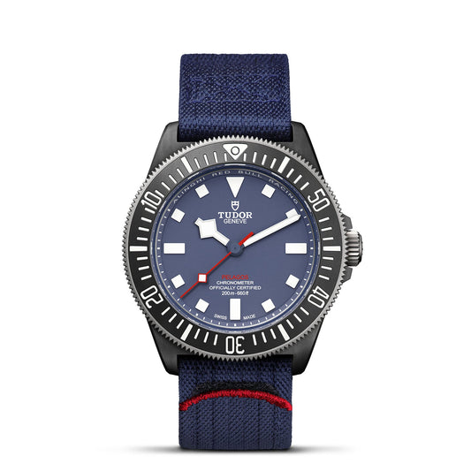 The TUDOR Pelagos FXD is a specialized diving watch featuring a blue dial with white hour markers and the "TUDOR" logo on display. Its blue textile strap, highlighted with a red accent, pairs perfectly with the metallic bezel and case to create an elegant appearance.