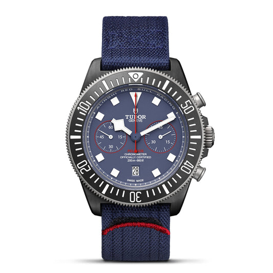 The TUDOR Pelagos FXD Chrono is a luxury wristwatch designed for yacht racing. It showcases a blue dial with white markings, complemented by a blue fabric strap. This watch features two subdials, a date window at 6 o'clock, and eye-catching red accents on both the strap and the bezel.