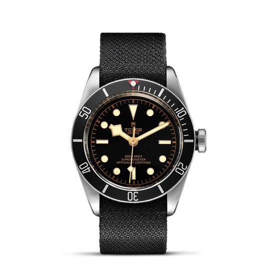 The TUDOR New Old Stock Black Bay wristwatch features a black dial, luminous markers, silver bezel, and iconic snowflake hands. Its fabric strap enhances the design with white numbering on the bezel, elegantly displaying hours, minutes, and seconds.