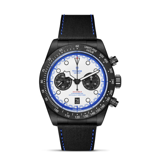 The TUDOR Black Bay Chrono “Carbon 25” is a boutique-exclusive chronograph with a white dial, TUDOR Blue accents, two black subdials, black leather strap with blue stitching, tachymeter bezel, and date window at 6 o’clock.