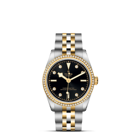 The TUDOR Black Bay One 31 S&G is a luxury watch with a black dial, gold hour markers, diamond-adorned gold bezel, date window at 3 o'clock beneath the logo, and a sleek Black Bay design complemented by a steel and yellow gold bracelet.