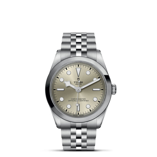 The TUDOR Black Bay One 36 wristwatch features a 36mm steel case, metallic bracelet, and round beige face. It includes simple hour markers, a date function, two hands, and reads "Tudor Genève Chronometer Officially Certified.