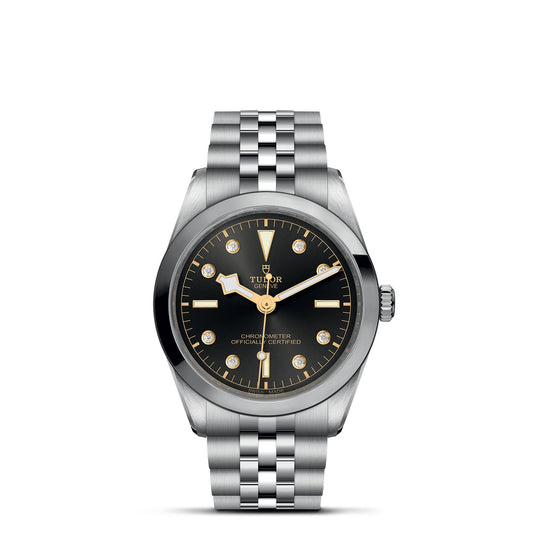 The TUDOR Black Bay One 36 features a luxurious design, with a silver metal band and black dial accented by gold hour markers and hands. Its 36mm stainless steel case and bezel reflect elegance. The watch face reads "Chronometer Officially Certified," inspired by TUDOR divers' watches.