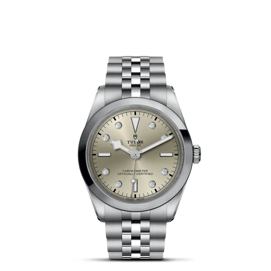 The TUDOR Black Bay One 36 is a silver wristwatch with a polished bezel, metallic bracelet, beige dial, silver hands, "Tudor Geneve" text, and a 36mm steel case that epitomizes the elegance of TUDOR divers' watches.