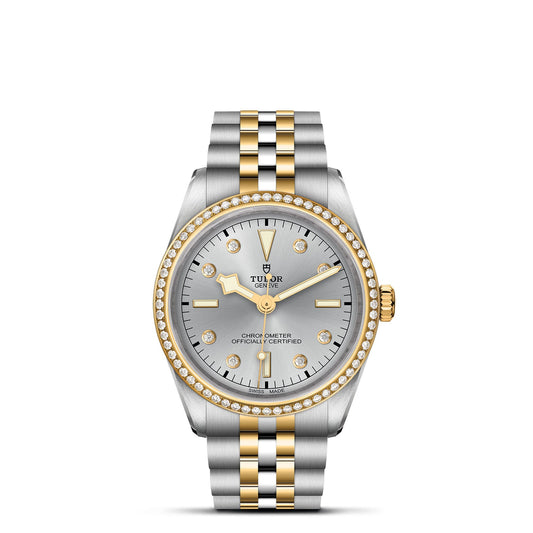 The TUDOR Black Bay One 36 S&G luxury watch features a 36mm steel case with a silver and gold two-tone band. It has a round silver face with gold hour markers, some adorned with diamonds, and gold hands. The diamond-encrusted bezel complements the refined TUDOR style, and "Chronometer Officially Certified" is displayed.