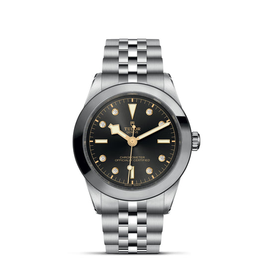 The TUDOR Black Bay One 39 features a silver stainless steel case and bracelet with a black dial and gold accents, reminiscent of the iconic design. Gold hour markers and hands enhance the style, while "TUDOR" is elegantly displayed on the dial, reflecting its diving watch heritage.