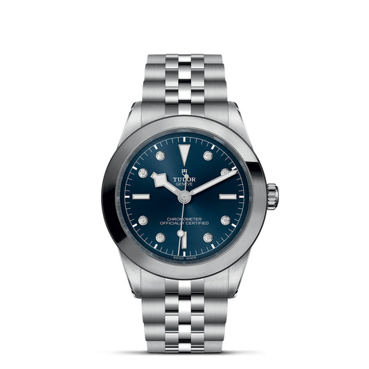 The TUDOR Black Bay One 39 features a 39mm steel case with a silver metal bracelet and striking blue dial. Silver hour markers, hands, and a date window enhance its elegance, while the iconic TUDOR logo graces the space below 12 o'clock.