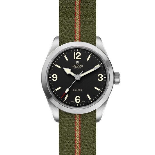 The TUDOR Ranger wristwatch boasts a green fabric strap adorned with a vivid red stripe and is accented by a silver bezel. Its black dial is elegantly highlighted by white hands, numerals, and markers beneath the esteemed TUDOR Geneva logo. Perfectly crafted for expeditions, this watch seamlessly merges durability with classic sophistication.