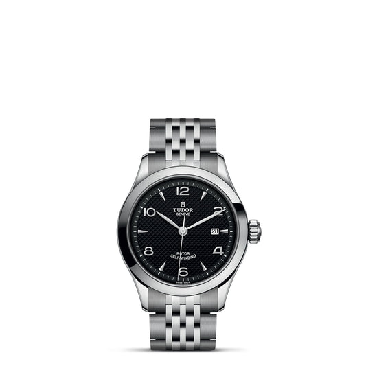 A TUDOR 1926 watch in silver showcases a black textured dial with white numerals and hands, complemented by a date display at the 3 o'clock position. It features a classic and elegant five-link metal bracelet, all presented against a plain white background.