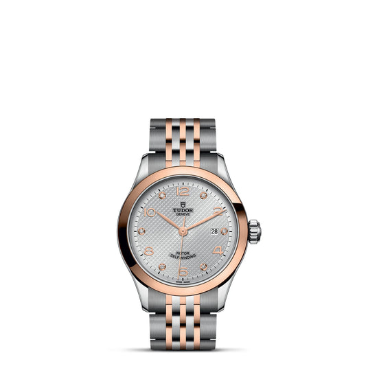 The TUDOR 1926 by TUDOR is a two-tone wristwatch with a silver and rose gold bracelet. This elegant timepiece features a silver textured dial adorned with rose gold hour markers and hands, along with a date window at the 3 o'clock position. The iconic Tudor logo is prominently displayed beneath the 12 o'clock marker, showcasing the sophistication of mechanical watches.
