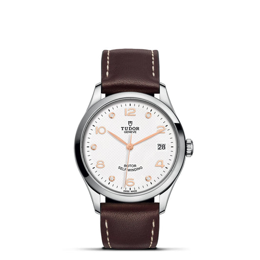 The TUDOR 1926 wristwatch showcases a white dial adorned with silver hour markers and is complemented by a brown leather strap. This sophisticated timepiece includes a date display at the 3 o'clock position and features "Rotor Self-Winding" near the 6 o'clock mark, highlighting the brand TUDOR's dedication to crafting exquisite mechanical watches.