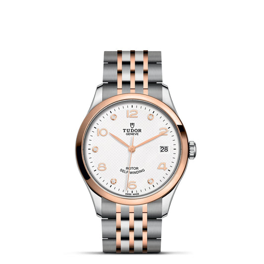 The TUDOR 1926 wristwatch showcases a two-tone metal strap in silver and rose gold. It features a round white dial with silver and rose gold hour markers, a date window at 3 o'clock, and proudly displays the TUDOR brand name. The rose gold bezel beautifully contrasts with the streamlined silver case.
