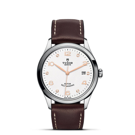 This sophisticated TUDOR 1926 wristwatch from the esteemed Tudor Geneve collection boasts a white dial adorned with rose gold hour markers and hands, along with a date display at 3 o'clock and the "ROTOR SELF-WINDING" inscription. It is complemented by a silver bezel and a brown leather strap featuring white stitching.