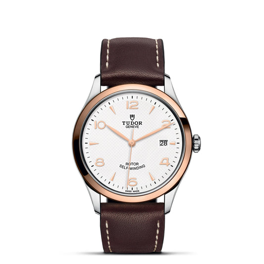 The TUDOR 1926, a stylish wristwatch from the brand TUDOR, showcases a white dial accented with gold hour markers and hands, as well as a date window positioned at 3 o'clock. Its case blends silver and gold tones beautifully, paired with a brown leather strap featuring visible stitching.