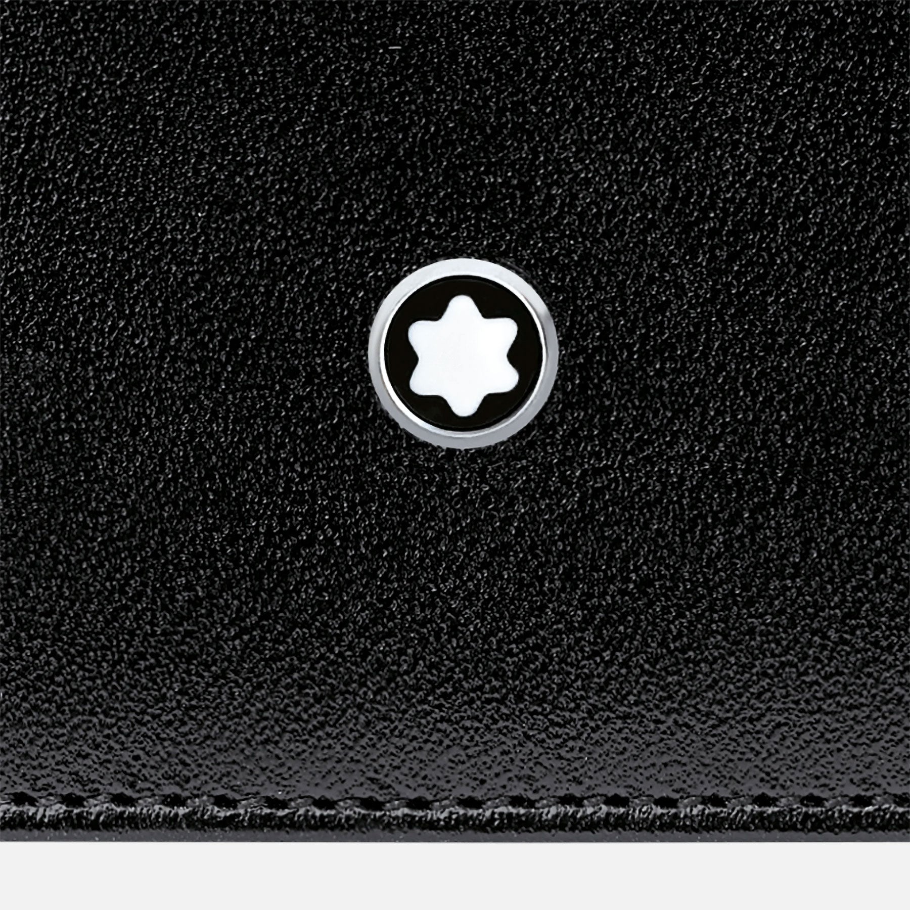 Close-up of the Montblanc Meisterstück Pocket 6cc Leather Card Holder's black calfskin leather surface with a circular logo. The logo displays a white six-pointed star inside a black circle, outlined with silver, reflecting a minimalist and elegant design characteristic of the esteemed Meisterstück collection by Montblanc.