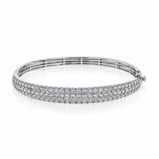 A sleek Simon G. 18K White Gold Three Row Diamond Bangle, adorned with rows of sparkling white diamonds, is displayed on a reflective surface. Its elegant design includes a secure clasp and smooth, rounded shape, enhancing its luxurious appearance. Crafted from 18k white gold by Simon G., it exudes timeless sophistication.