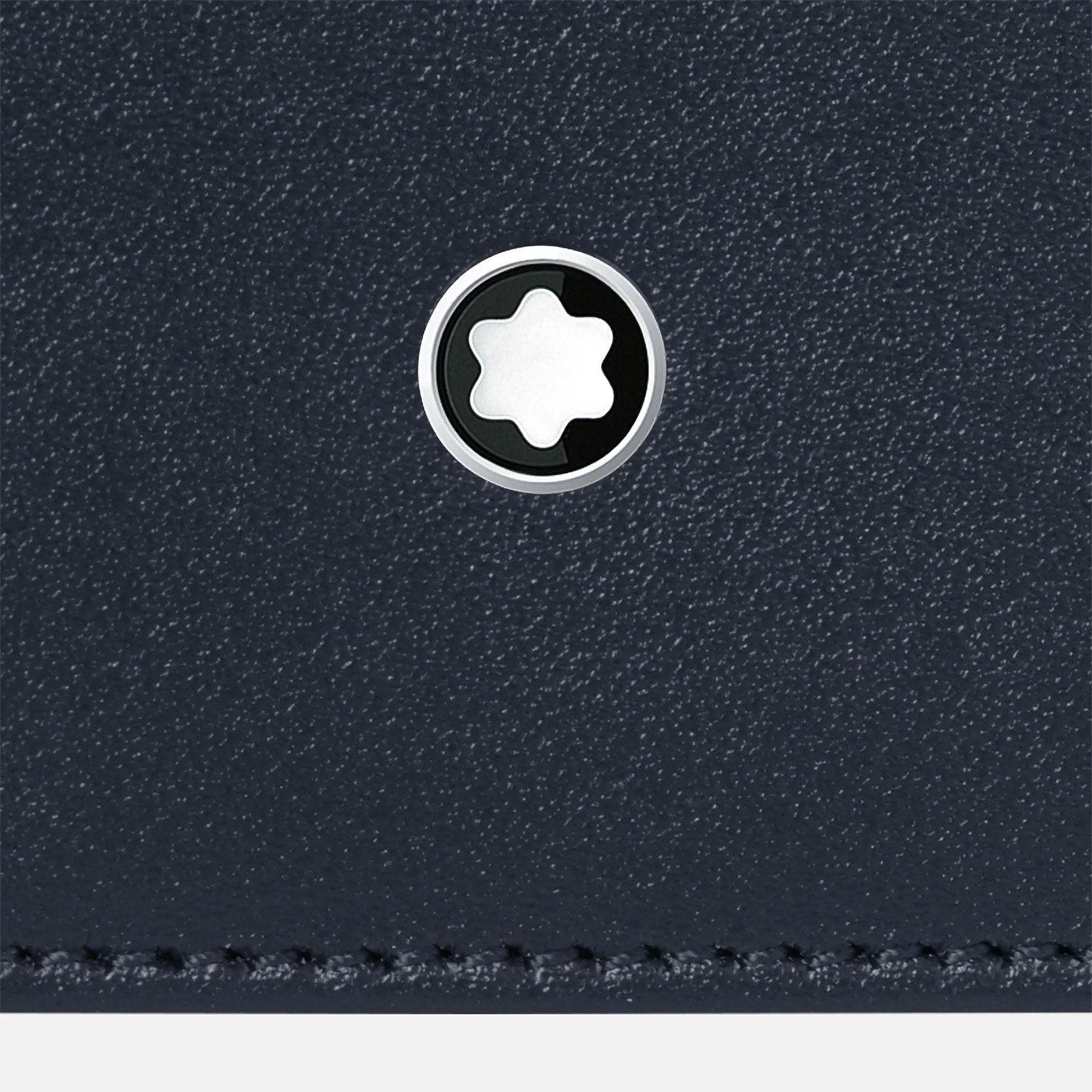 A close-up of the Montblanc Meisterstück Leather Wallet 6cc reveals a textured black leather surface adorned with a circular metallic emblem, prominently featuring a six-pointed star at its center. The stitching along the bottom edge adds a subtle detail to its modern design, making this Montblanc essential a must-have for any collection.