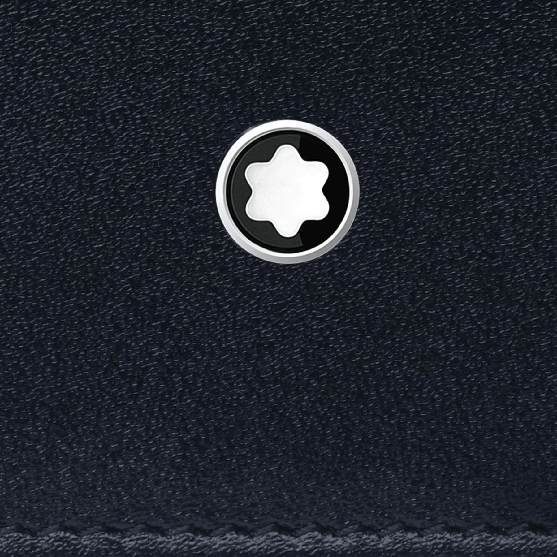 Close-up of the textured black leather surface of the Montblanc Meisterstuck Pocket 6cc Leather Card Holder, featuring a small circular emblem. The emblem includes a white six-pointed star within a black circle, offering a contrasting and elegant design. This lightweight Montblanc accessory perfectly combines style and function.