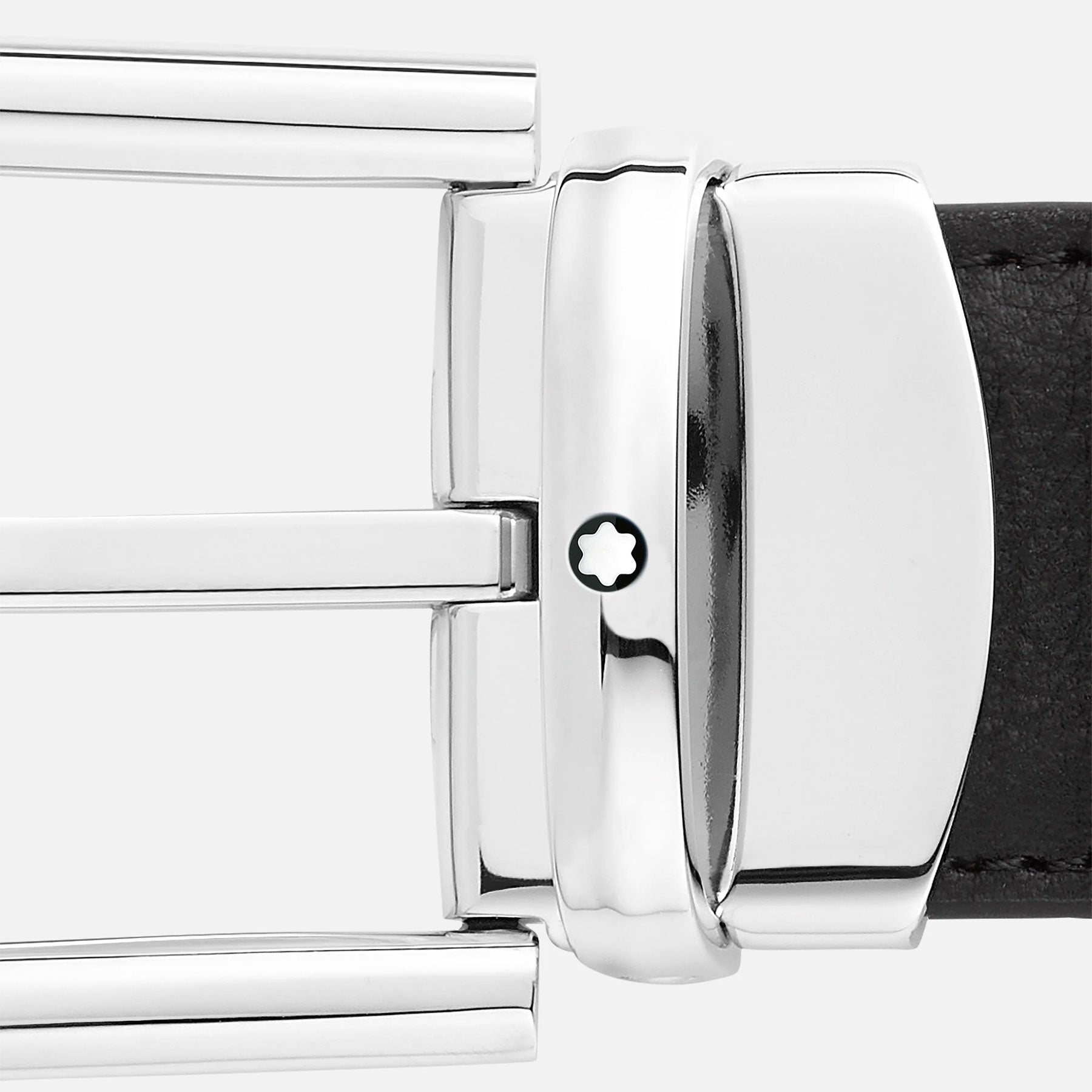 A close-up reveals the refined metallic buckle of the Montblanc Horseshoe Leather Belt, showcasing a polished palladium finish adorned with a distinctive white star emblem. The black leather belt, branded by Montblanc, is partially visible to the right side of the buckle against a light gray backdrop.