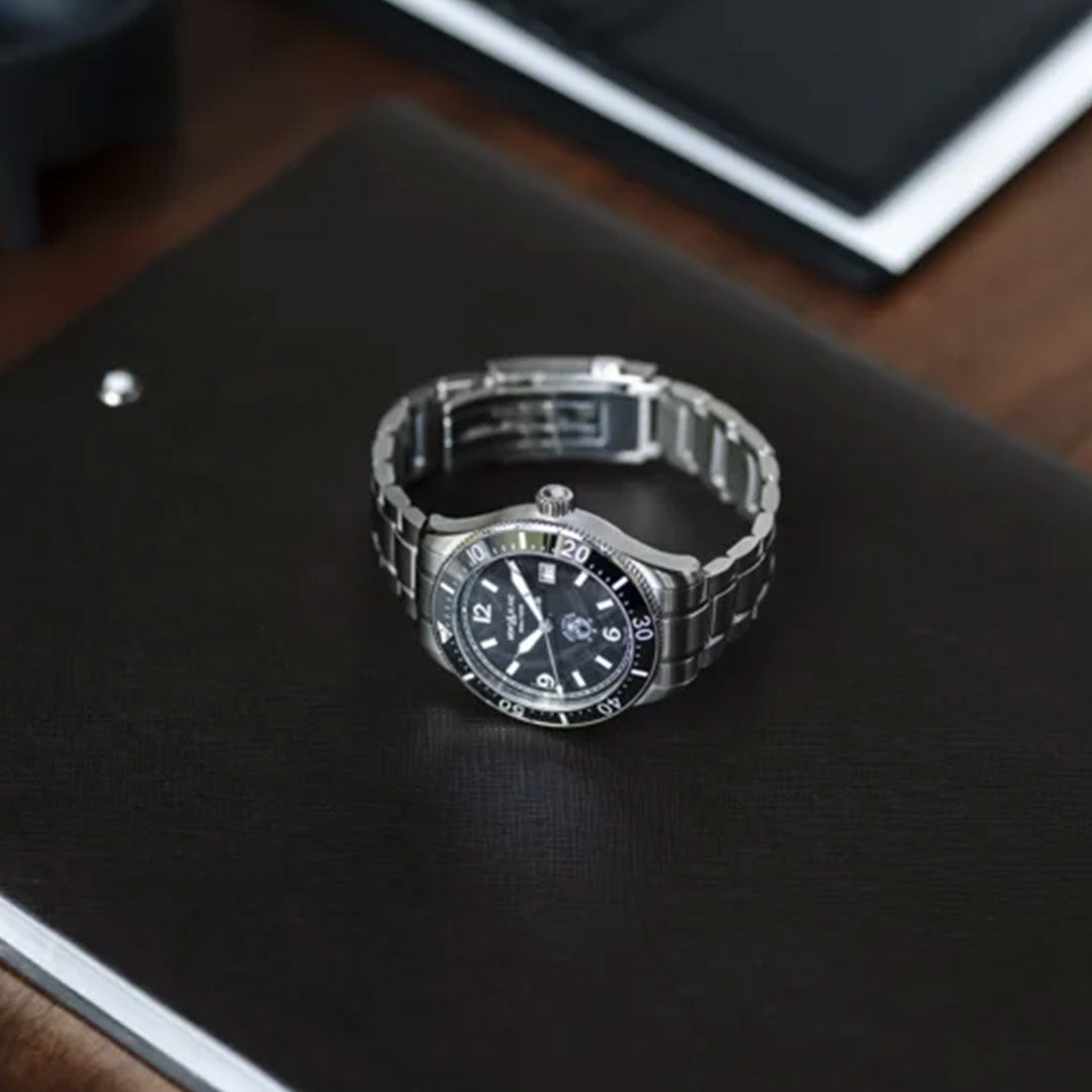 A Montblanc Iced Sea Automatic 41mm Watch, featuring a glacier pattern dial and classic three-hand design, rests on a closed dark-colored notebook placed on a wooden surface.