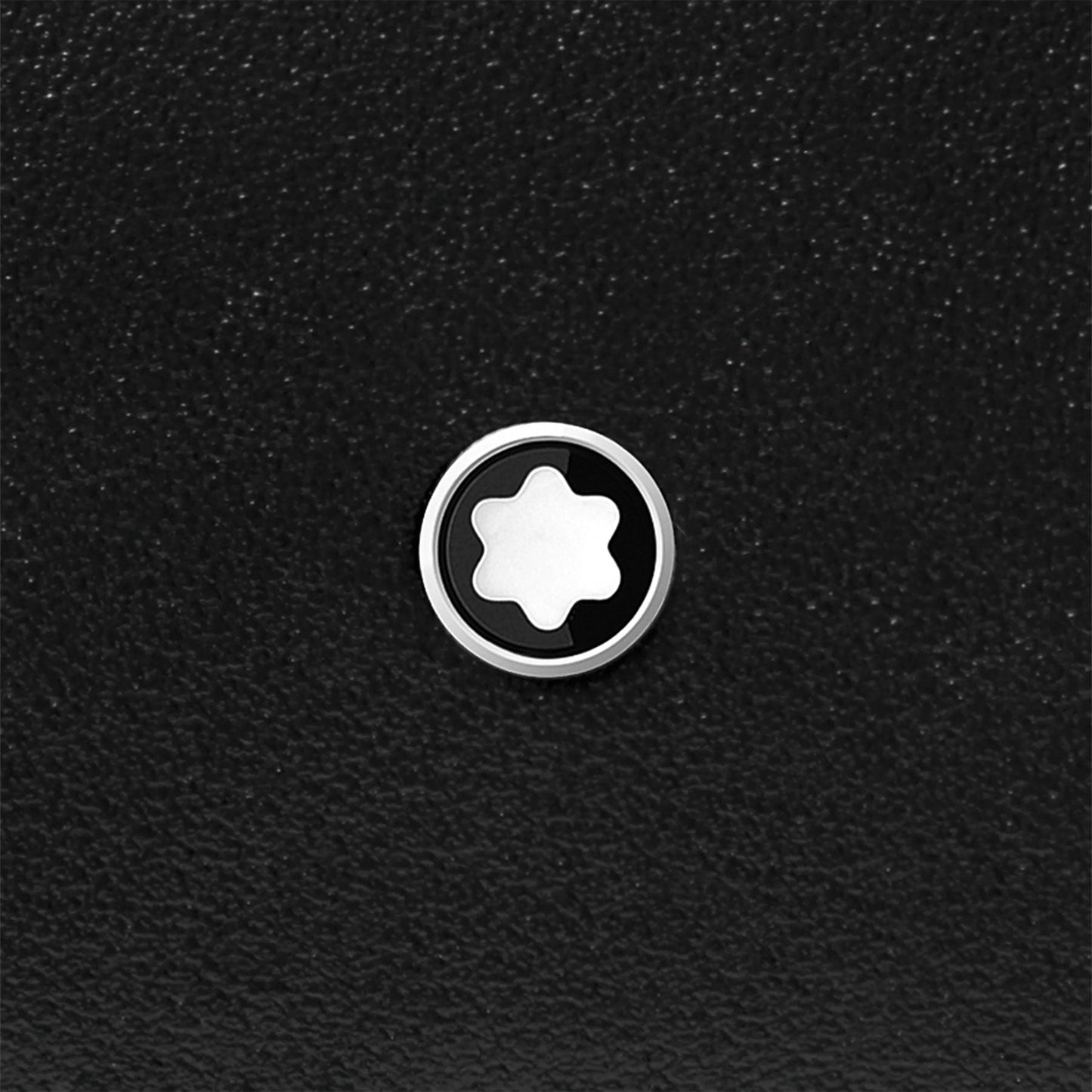 A circular logo with a white star-like design inside a black circle is prominently displayed against a textured black background, evoking the timeless sophistication of the Montblanc Meisterstück Compact Black Leather Wallet 6cc.